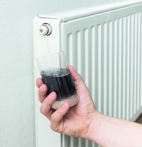 Glass of dirty heating water in front of a radiator
